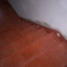 Schody wyłożone pomarańczowo-brązowymi płytkami ceramicznymi z widocznymi otworami na oświetlenie punktowe w ścianie w trakcie remontu.